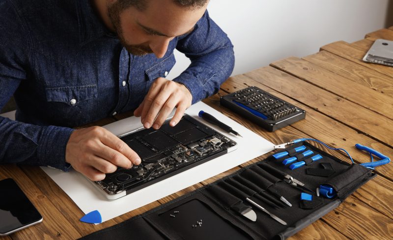 Master uses angled esd tweezers to remove dust from electronic boards of broken slim computer laptop to fix it and make to work again